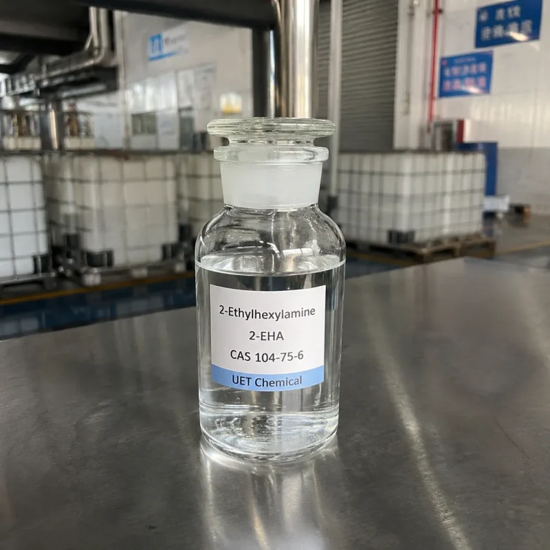2-eha-2-ethylhexylamine-sample-bottle-clear-liquid Clear glass reagent bottle filled with colorless liquid 2-Ethylhexylamine (2-EHA, CAS 104-75-6) on stainless steel table, labeled UET Chemical, IBC tanks visible in factory background