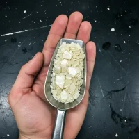 2-naphthol-crystals-cas-135-19-3-flake-appearance-scoop Macro close-up of creamy white 2-Naphthol Crystals CAS 135-19-3 flakes in a stainless steel scoop, showcasing its pure physical appearance and flake texture for dye synthesis and rubber intermediates.