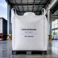 calcined-bauxite-ibc-ton-bag-packaging-warehouse White IBC ton bag of Calcined Bauxite CAS 1318-16-7 with UET Chemical branding, placed on a black plastic pallet in a modern warehouse, suitable for large-scale industrial supply.