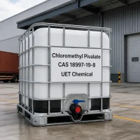 White IBC tote of Chloromethyl Pivalate CAS 18997-19-8 with metal cage and discharge valve outside factory, label showing UET Chemical branding.