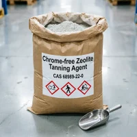 chrome-free-zeolite-tanning-agent-25kg-bag A 25kg kraft paper bag of Chrome-free Zeolite Tanning Agent (CAS 68989-22-0) with an open top, revealing its fine powder inside. The front label carries GHS safety pictograms for secure handling, with a metal scoop resting on the floor beside it, ready for sampling.