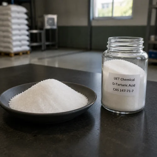 d-tartaric-acid-white-crystal-powder-sample-metal-dish White crystalline powder of D-Tartaric Acid (CAS 147-71-7) displayed in stainless steel dish beside clear glass reagent bottle on dark lab surface, labeled UET Chemical, sample for purity and physical property verification