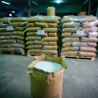 eva-copolymer-granules-open-bag-warehouse-stock Open kraft paper bag showing white EVA copolymer granules ready for industrial compounding, stored in a warehouse with stacked 25kg sacks in the background.
