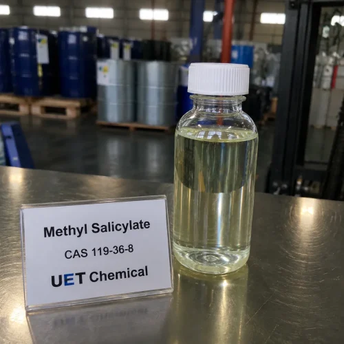 methyl-salicylate-cas-119-36-8-liquid-sample-bottle-u-et-chemical Clear plastic sample bottle containing pale yellow liquid Methyl Salicylate (CAS 119-36-8) next to a display card on stainless steel surface, labeled UET Chemical, sample for flavor, fragrance or pharmaceutical grade raw material