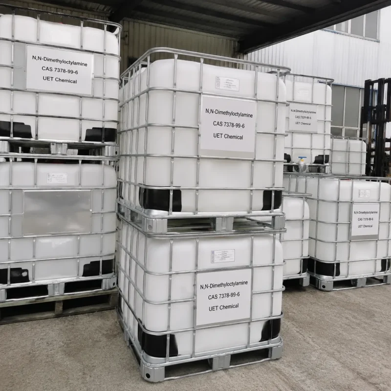 n-n-dimethyloctylamine-dma8-ibc-tote-bulk-storage Stacked white IBC totes (Intermediate Bulk Containers) with metal cages containing N,N-Dimethyloctylamine (DMA8, CAS 7378-99-6), labeled UET Chemical, bulk liquid storage at outdoor chemical warehouse