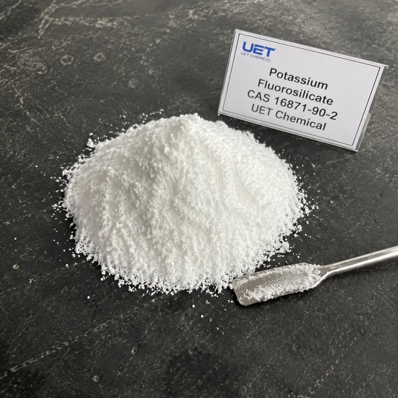 potassium-fluorosilicate-cas-16871-90-2-white-powder-sample Pile of fine white crystalline powder Potassium Fluorosilicate (CAS 16871-90-2) on dark stone surface with metal spatula, labeled UET Chemical, sample for glass, ceramic or enamel industry raw material verification