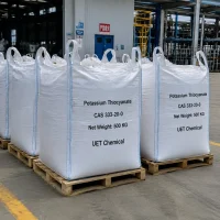 potassium-thiocyanate-kscn-500kg-ton-bag-industrial-pallet-factory Large white woven ton bags (Net Weight: 500 KG each) of Potassium Thiocyanate (KSCN, CAS 333-20-0) on wooden pallets in factory setting, labeled UET Chemical, industrial-grade bulk supply for large-scale manufacturing