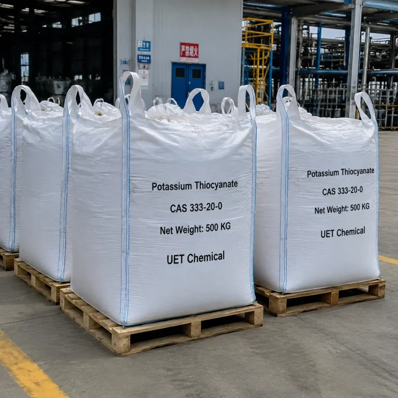 potassium-thiocyanate-kscn-500kg-ton-bag-industrial-pallet-factory Large white woven ton bags (Net Weight: 500 KG each) of Potassium Thiocyanate (KSCN, CAS 333-20-0) on wooden pallets in factory setting, labeled UET Chemical, industrial-grade bulk supply for large-scale manufacturing