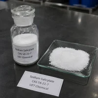 sodium-salicylate-white-powder-sample-glass-bottle Close-up of white crystalline powder Sodium Salicylate (CAS 54-21-7) in a clear glass reagent bottle with ground glass stopper, alongside a glass dish displaying the powder texture, labeled UET Chemical, product sample on a dark lab bench