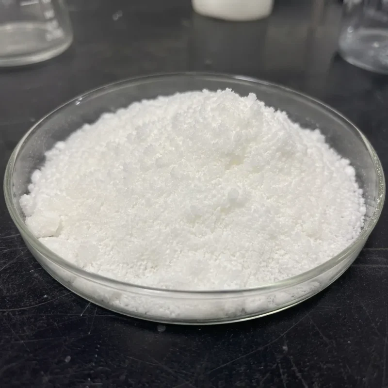sodium-stannate-trihydrate-cas-12209-98-2-white-crystal-sample White crystalline Sodium Stannate Trihydrate CAS 12209-98-2 sample in a glass petri dish, on a lab bench with glassware in the background.