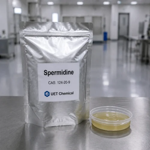 spermidine-cas-124-20-9-silver-foil-bag-sample A silver foil bag of Spermidine CAS 124-20-9 labeled UET Chemical, with a sample dish of pale yellow liquid beside it, on a stainless steel table in a clean lab environment.