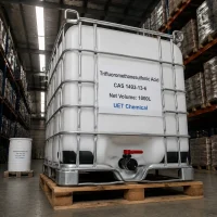 A 1000L white IBC tank of Trifluoromethanesulfonic Acid (Triflic Acid) CAS 1493-13-6 with metal cage frame and bottom valve on wooden pallet, labeled UET Chemical, in a warehouse setting.